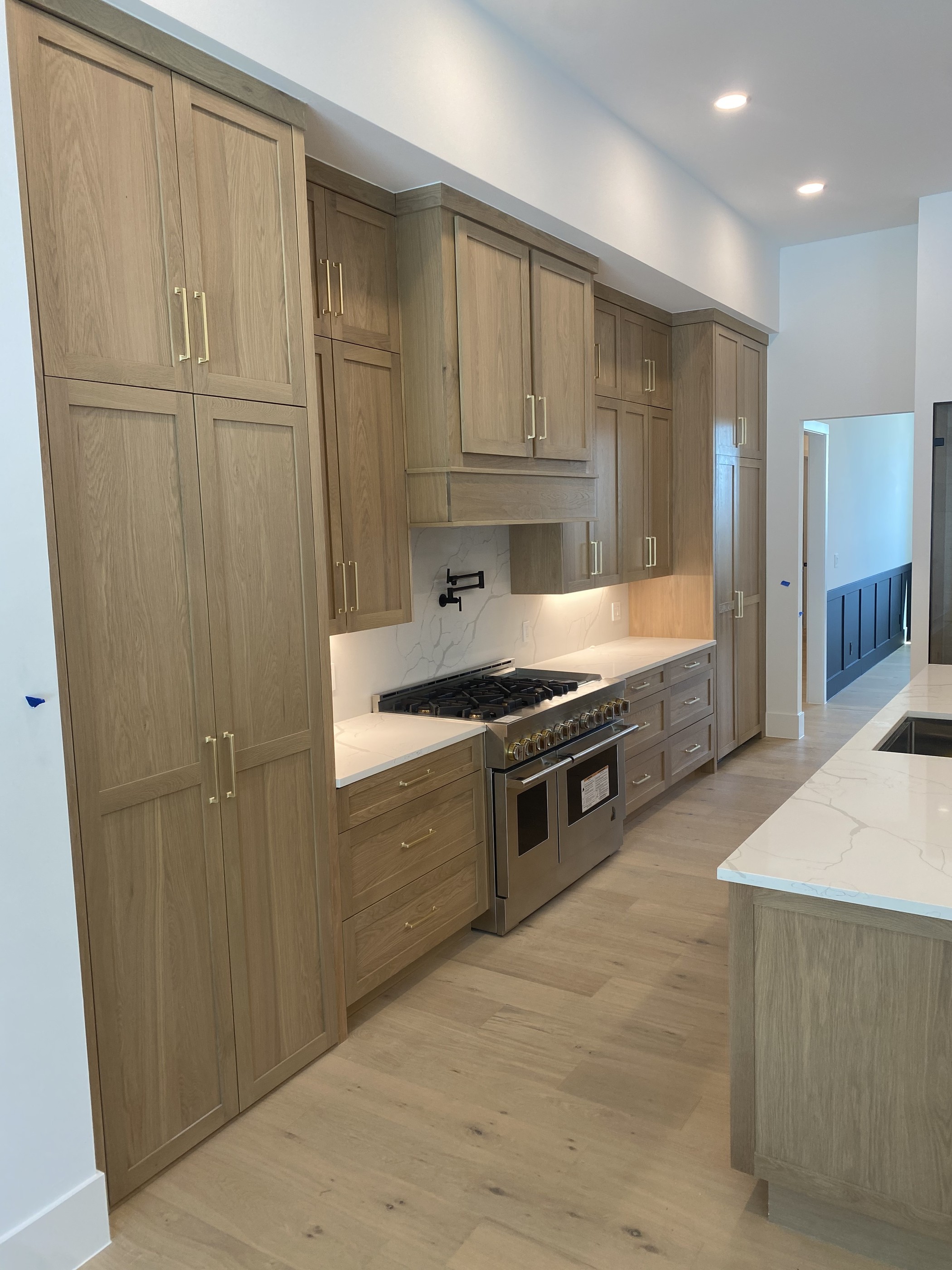 White oak shaker kitchen with marble backsplash and brass hardware